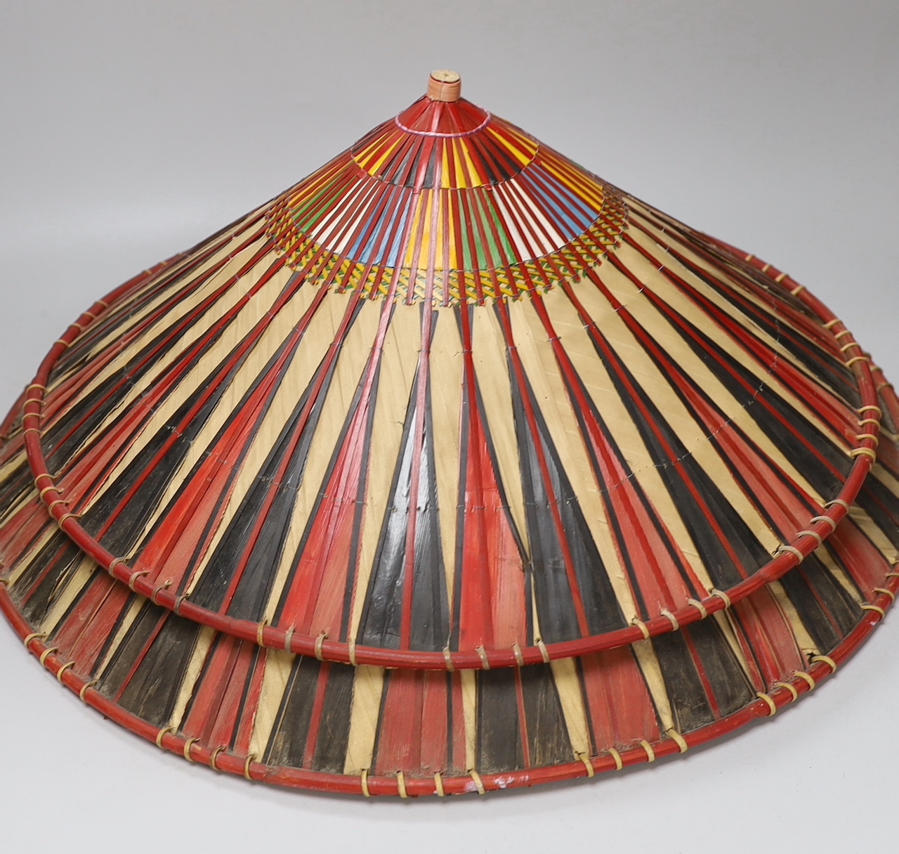 Three red and black striped bamboo rice hats, together with a smaller rice hat with beaded flag decoration